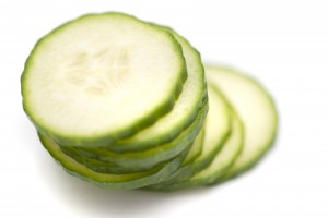 Stacked sliced cucumber with focus to the top slice showing the fleshy pulp and green rind on white